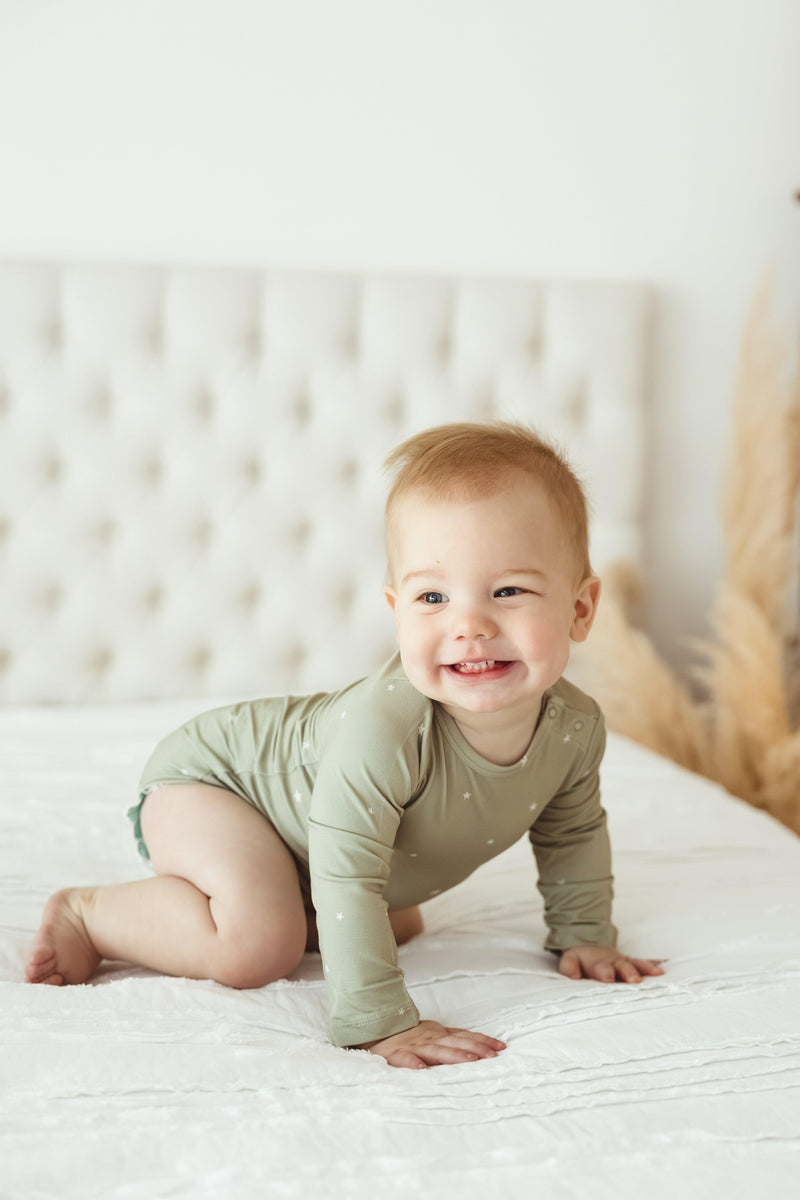 Candid photo of baby crawling in sage green star-print bamboo bodysuit, highlighting the flexible fabric and secure snap closure — perfect for active infants and toddlers.
