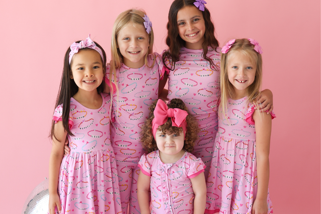 A group of little girls wearing Bamboo pajamas and twirl dresses with a friendship bracelet print. 