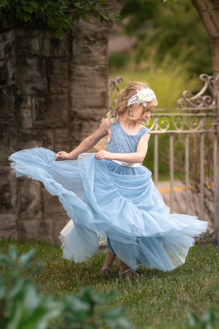 Young girl in a dusty blue flower girl dress twirling in front of a stone archway.
