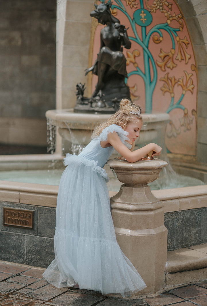 Girl in blue velvet princess dress beside a fairytale fountain