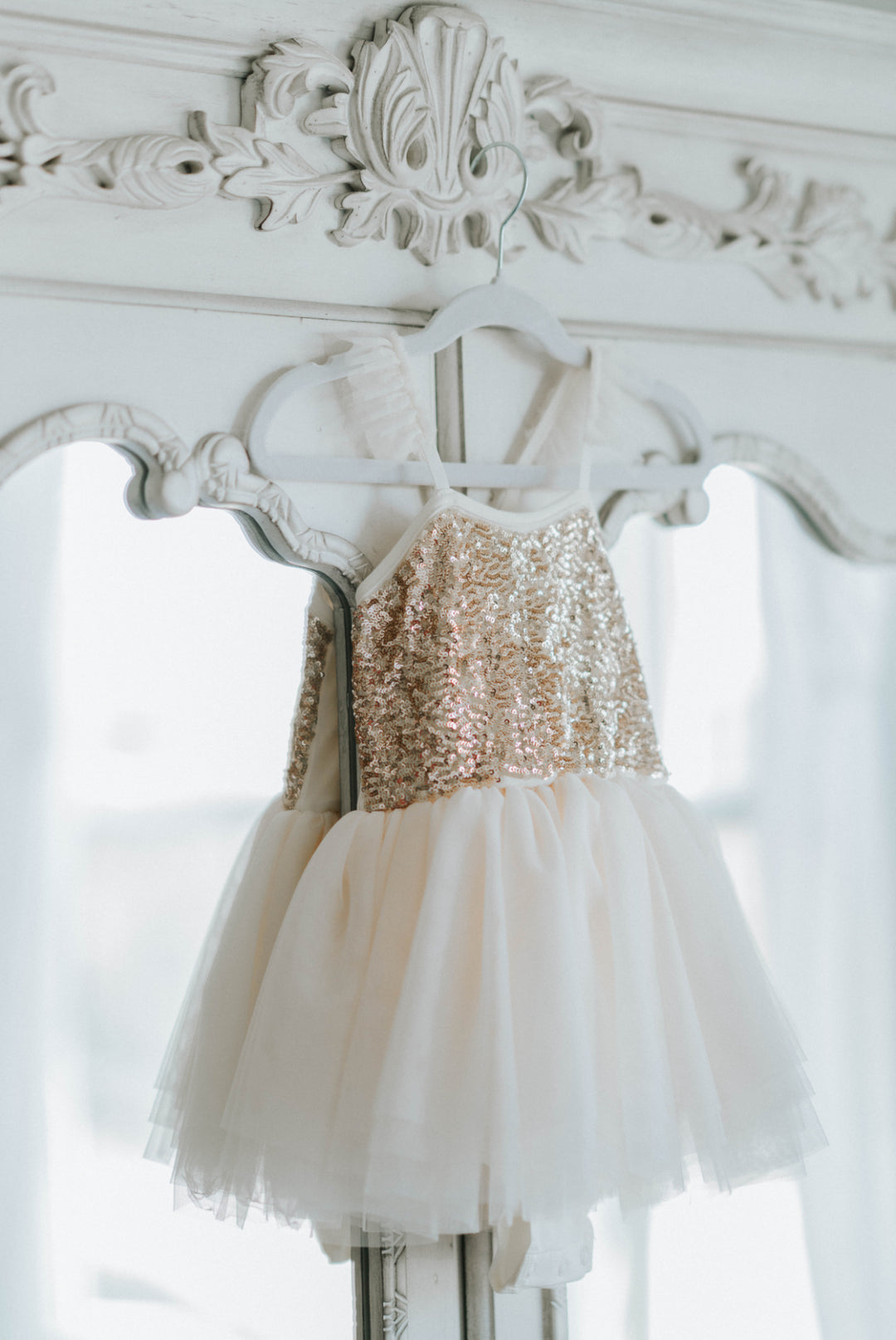 Cream and gold sequin tutu dress hanging on an ornate white mirror, layered tulle skirt displayed