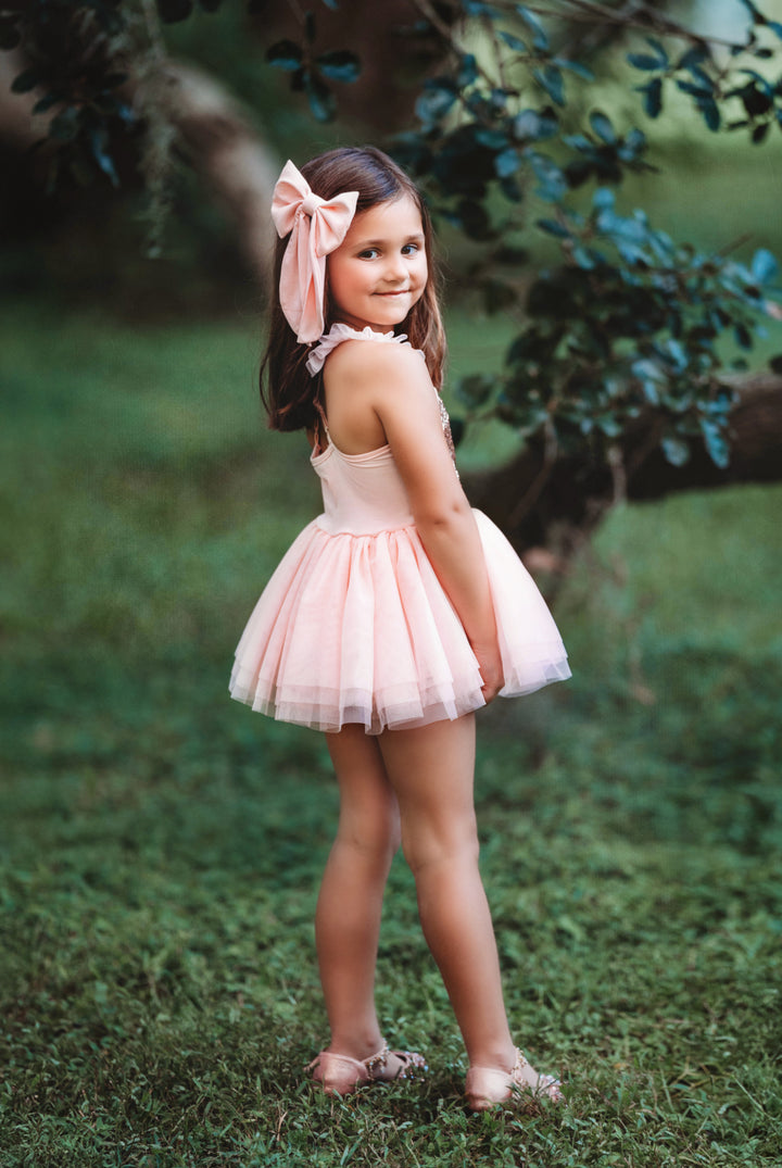 Back view of blush pink sequin tutu dress in outdoor garden setting.