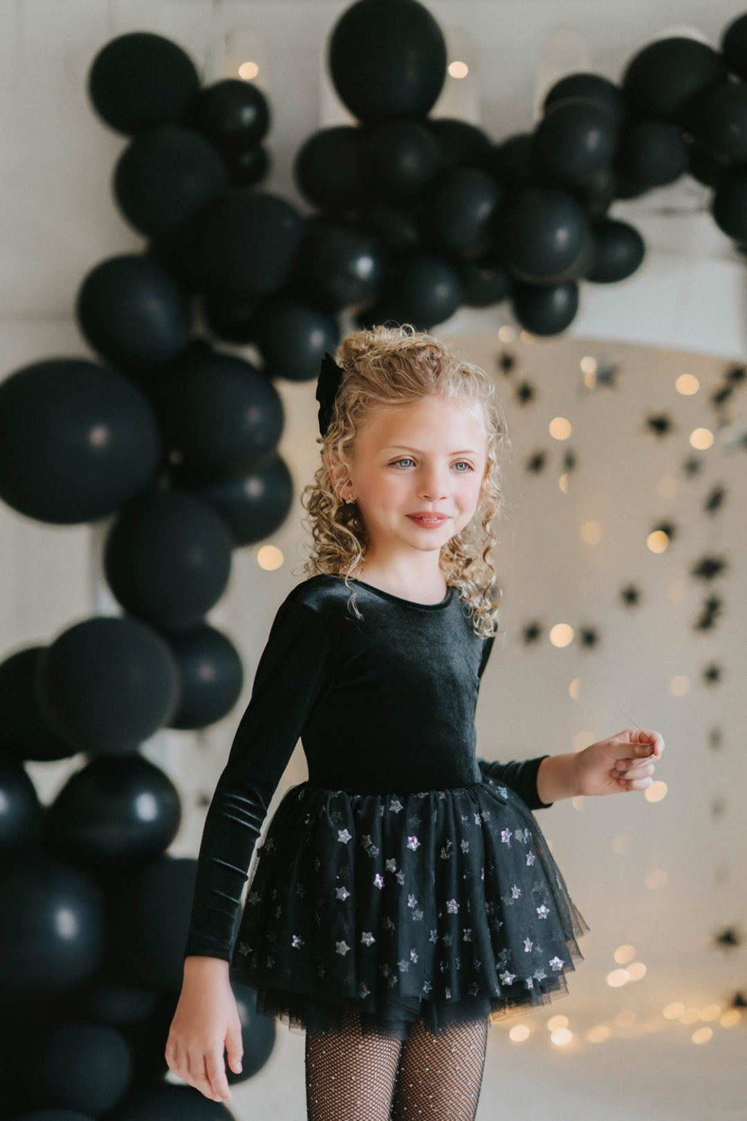 Girl in black velvet twirl dress with star tulle skirt in whimsical star photo backdrop.