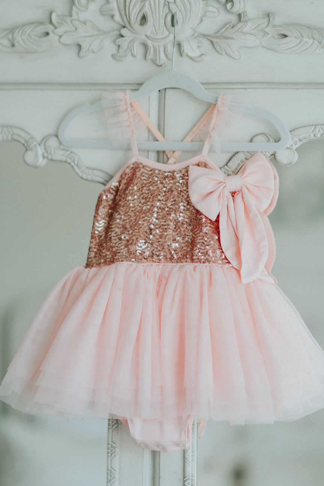 Pink sequin tutu dress hanging on white decorative hanger with bow detail.