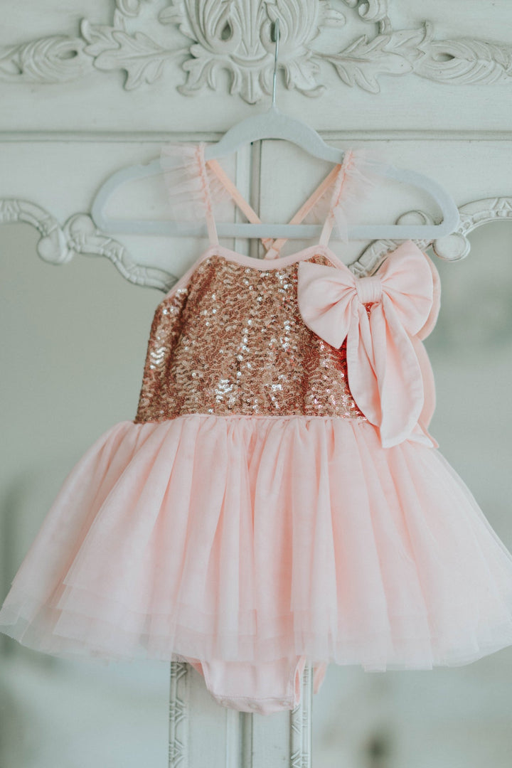 Pink sequin tutu dress hanging on white decorative hanger with bow detail.