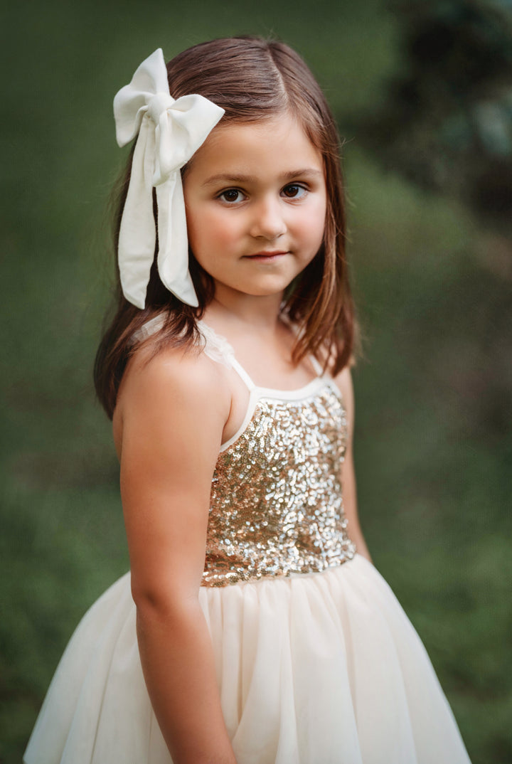 Child wearing cream and gold sparkle bodice tutu dress with oversized hair bow