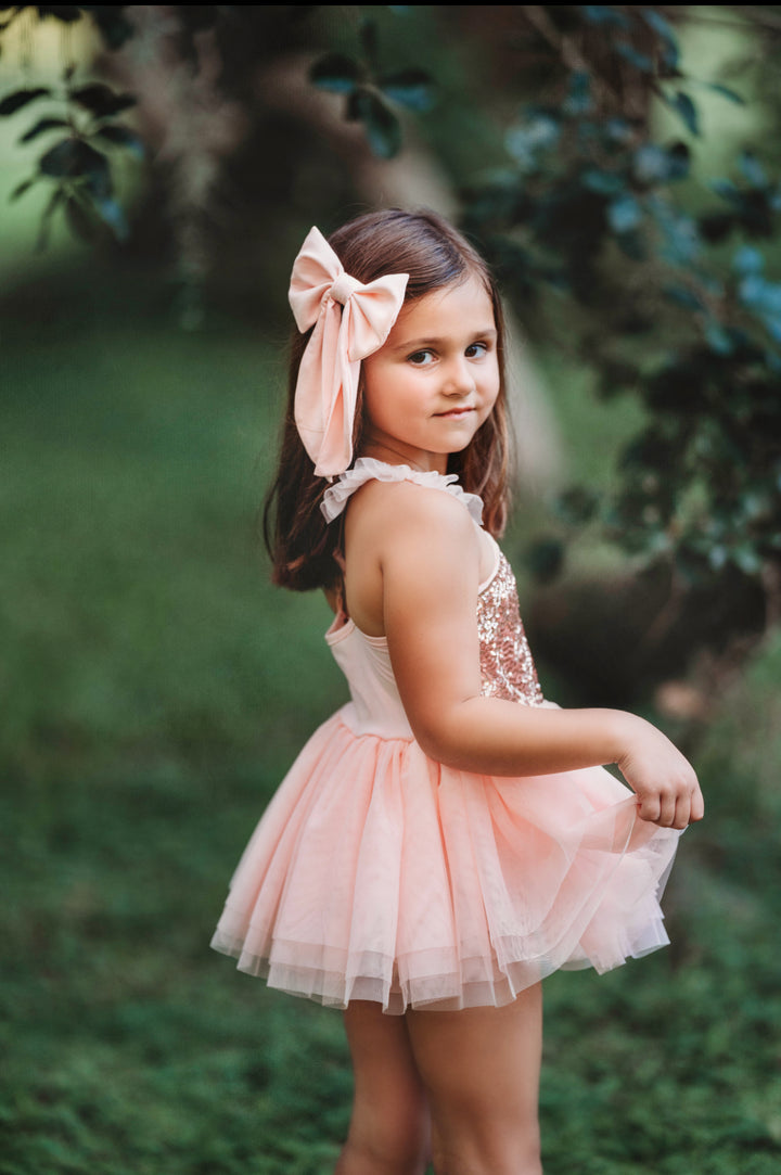 Girl wearing blush pink tutu dress with oversized bow in her hair.