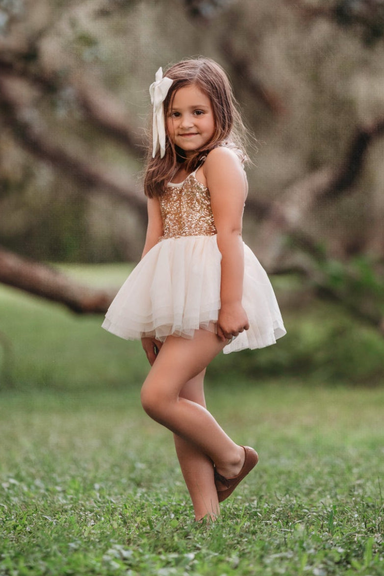 Close-up portrait of child wearing cream and gold sparkle bodice tutu dress with oversized hair bow