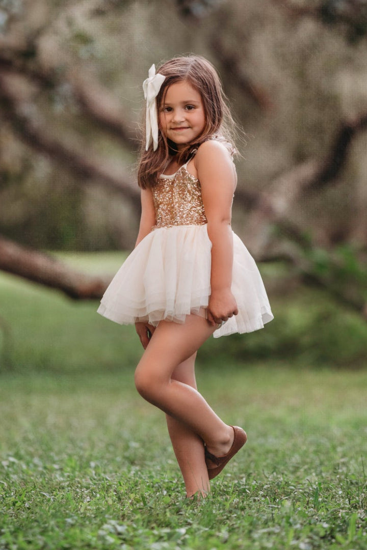 Close-up portrait of child wearing cream and gold sparkle bodice tutu dress with oversized hair bow