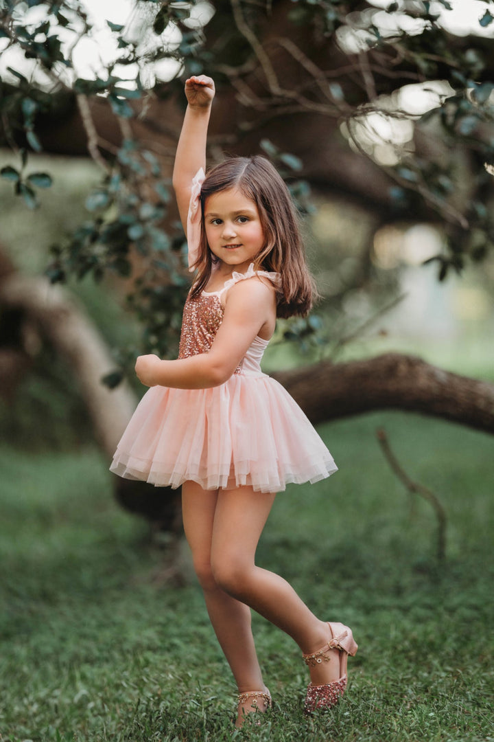 Girl spinning in blush pink sequin ballet-style tutu dress outside.