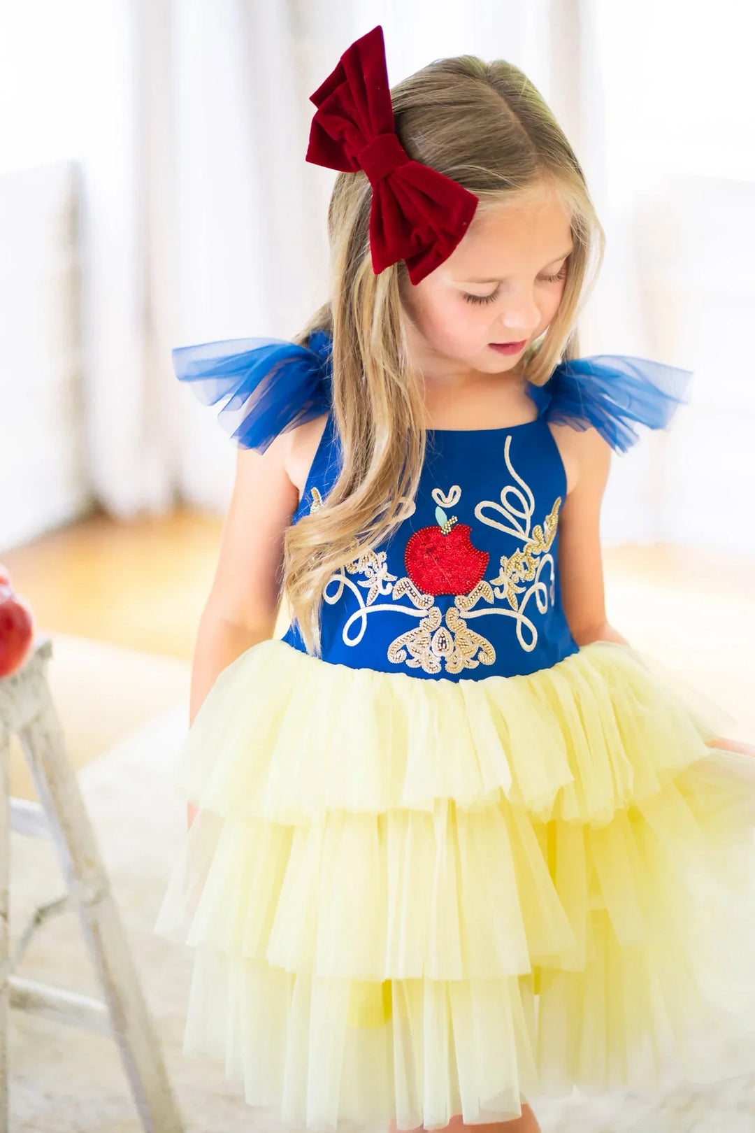 Girl wearing the Enchanted Apple princess dress with royal blue bodice and yellow tulle skirt inspired by Snow White