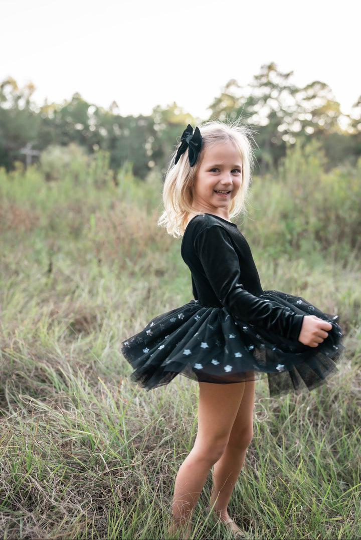 Girl wearing black velvet star tutu dress outdoors in field.