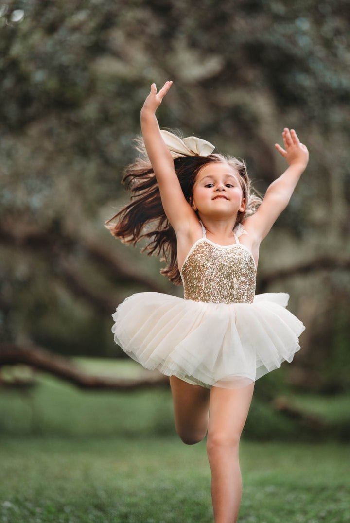 Toddler girl twirling in cream and gold tulle skirt dress, soft movement and playful pose outdoors