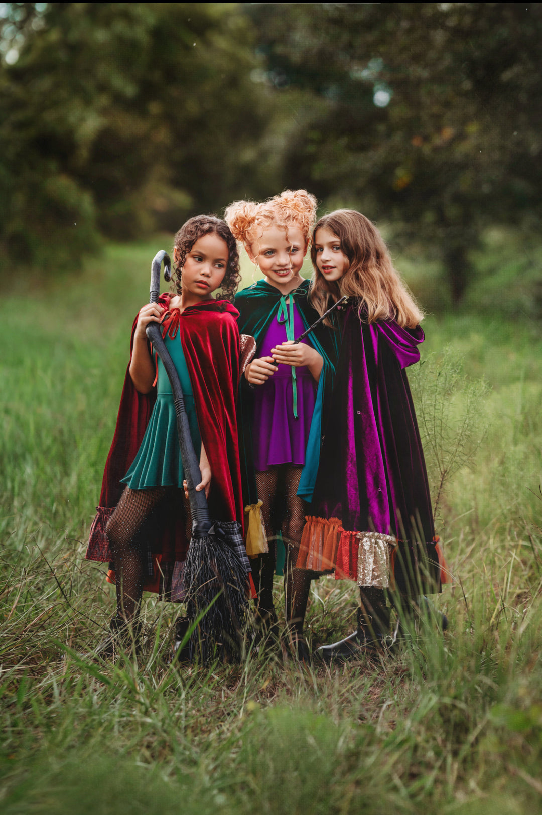 Three children together wearing green, red, and purple velvet witch costume capes inspired by winifred, sarah and Mary Sanderson from Hocus Pocus for halloween.