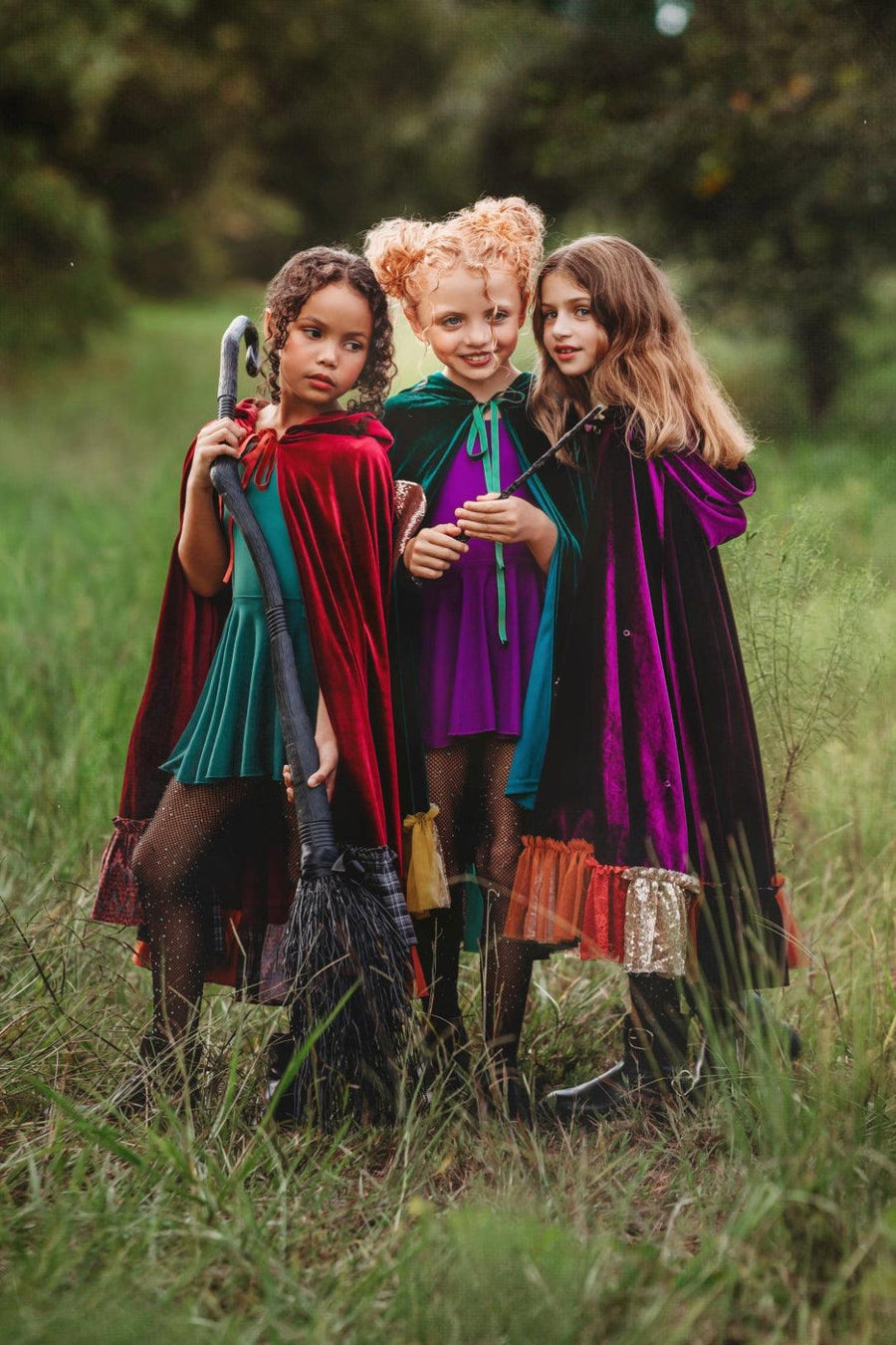 Three children together wearing green, red, and purple velvet witch costume capes inspired by winifred, sarah and Mary Sanderson from Hocus Pocus for halloween.