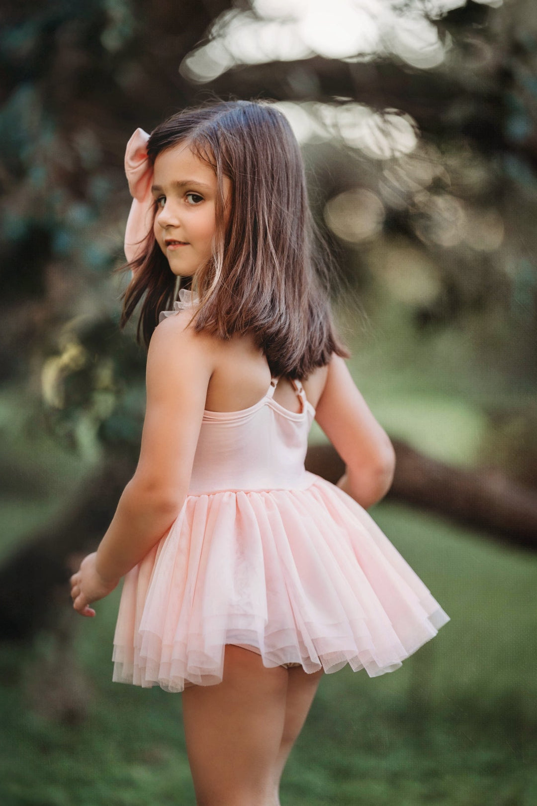 Little girl posing in pink sequin tutu dress, hands raised while dancing.