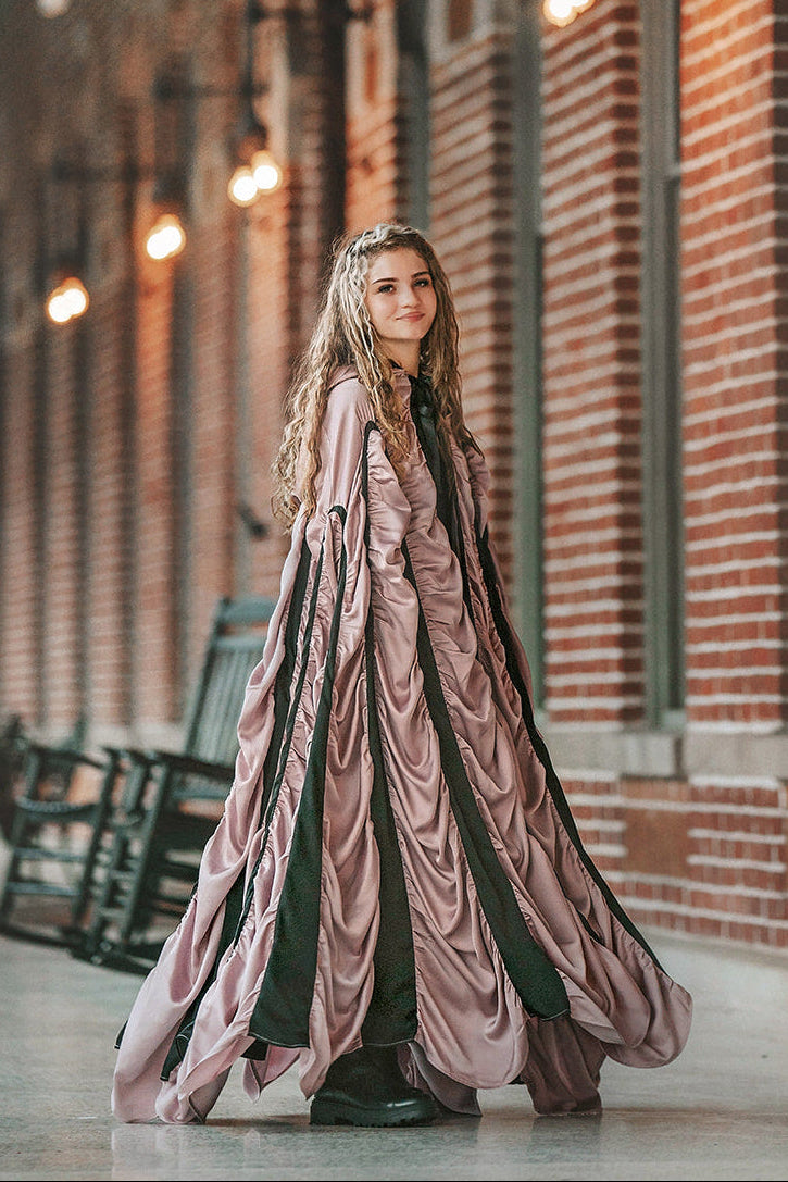 Woman wearing the mauve satin Coffin Cape with dramatic gathered folds, black trim and Gothic hood