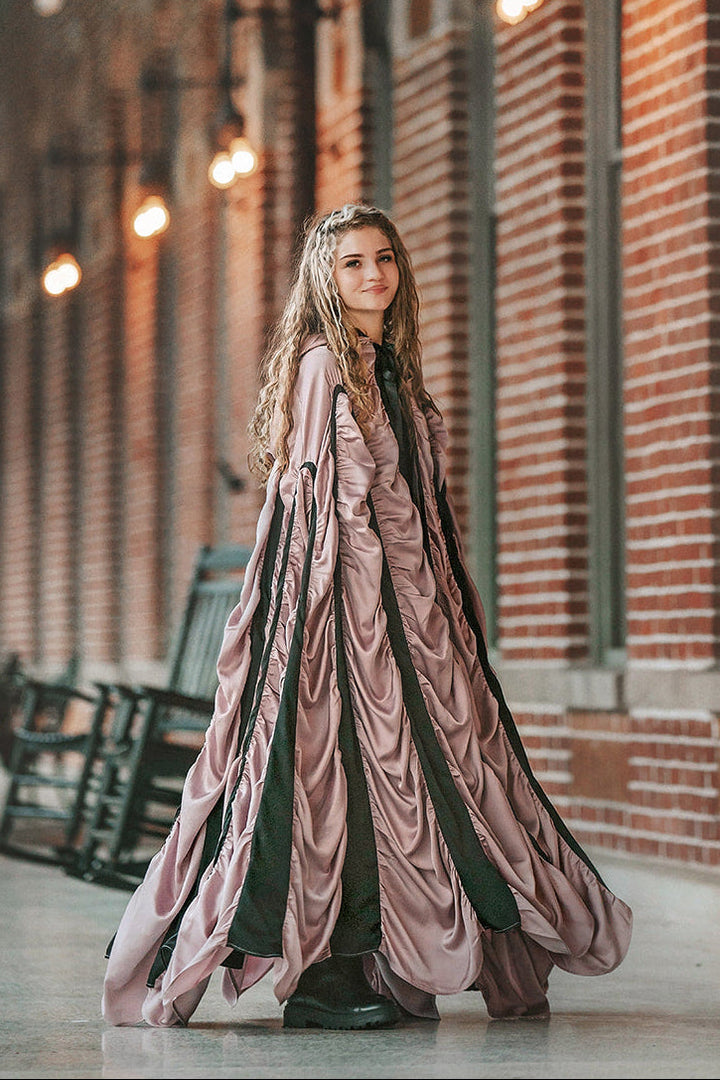 Woman wearing the mauve satin Coffin Cape with dramatic gathered folds, black trim and Gothic hood