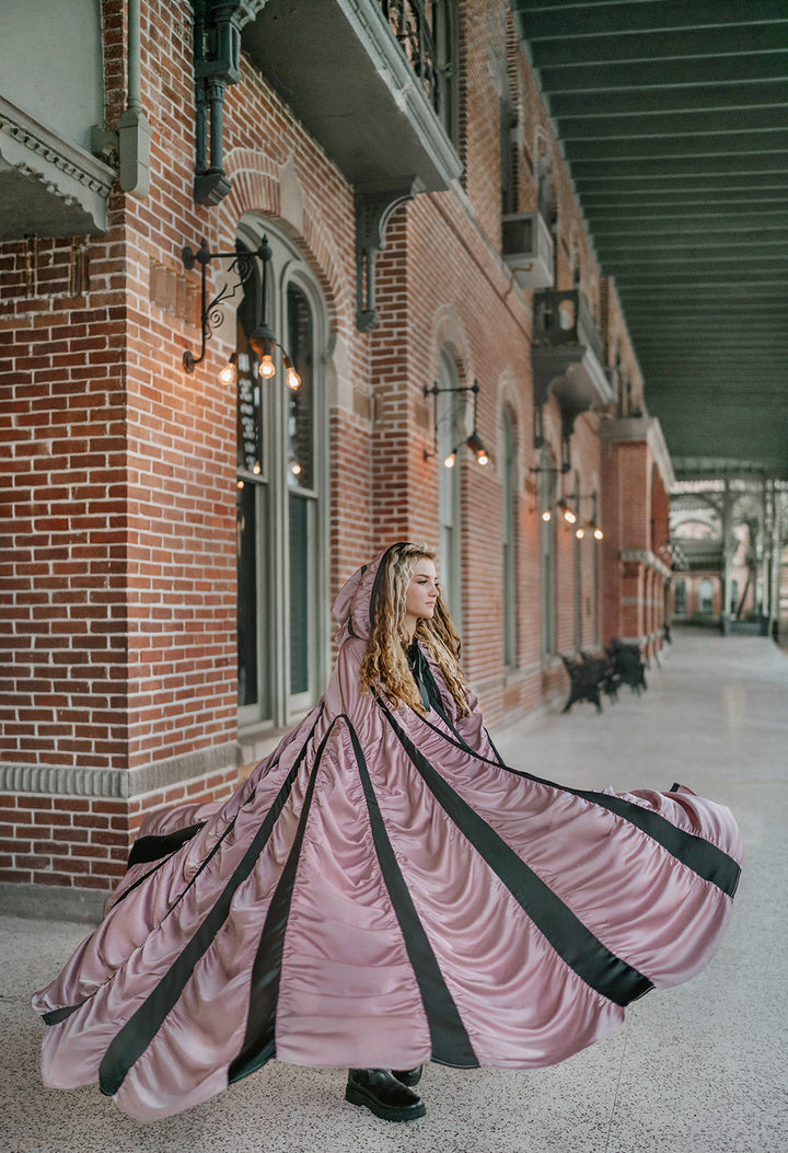 Mauve satin Coffin Cape fanned wide in motion, showing dramatic Gothic volume and contrasting black bands for Halloween.