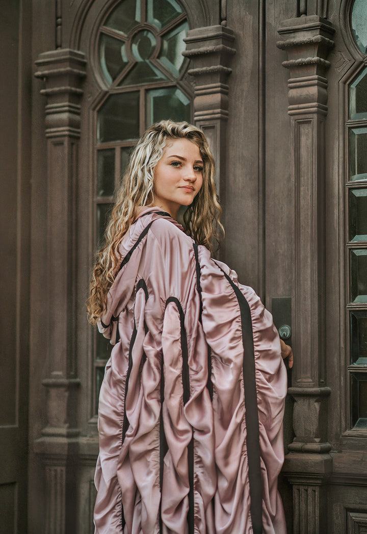 Woman wearing the mauve satin Coffin Cape Costume with dramatic gathered folds, black trim and Gothic hood