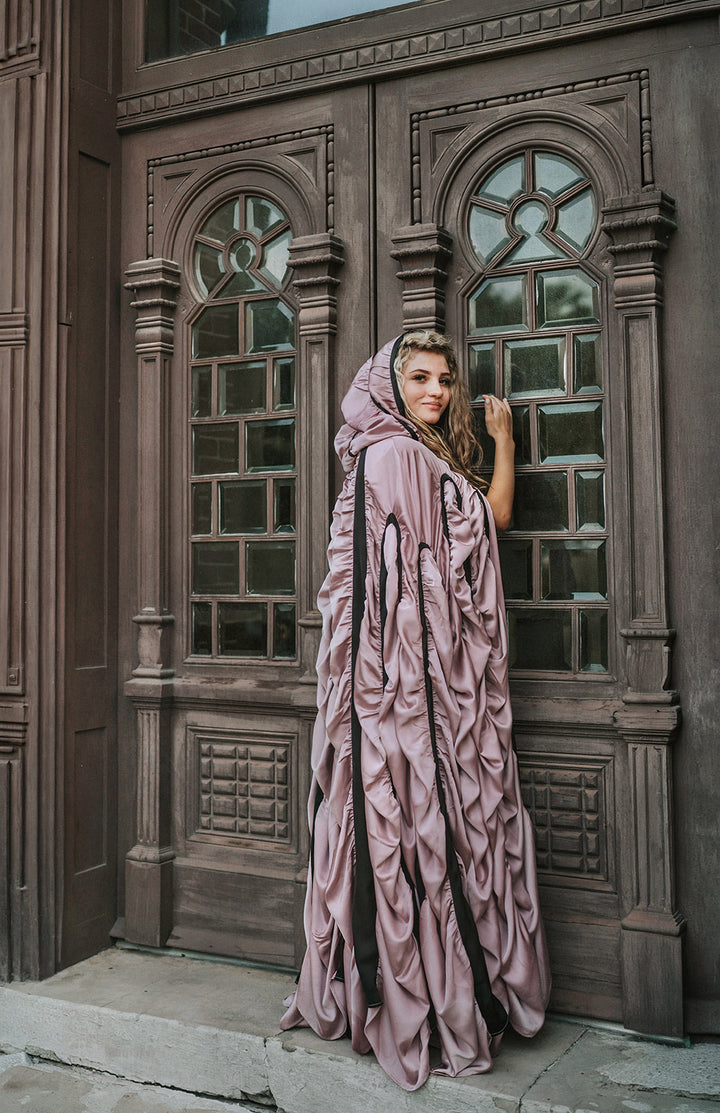 Back view of The Coffin Cape showing floor-length gathered mauve satin, black bands and draped hood