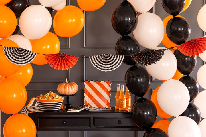 Halloween accordion fan garland styled above a party table with pumpkins balloons and orange black and white decorations
