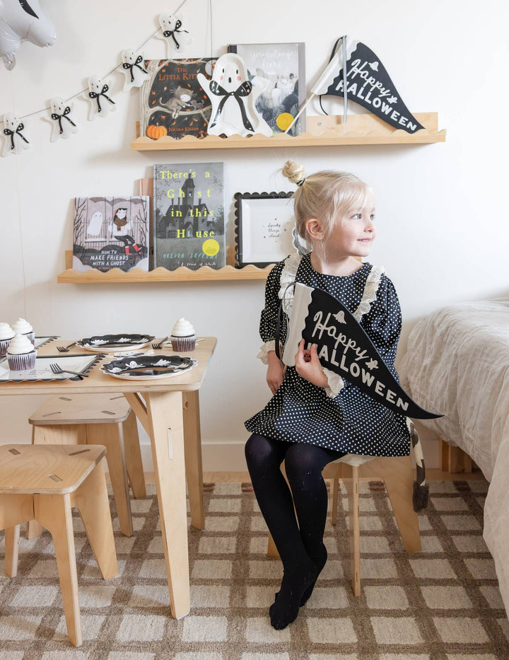 My Mind’s Eye felt ghost Halloween garland displayed on the wall as a little girl prepares a Halloween party and holding a banner