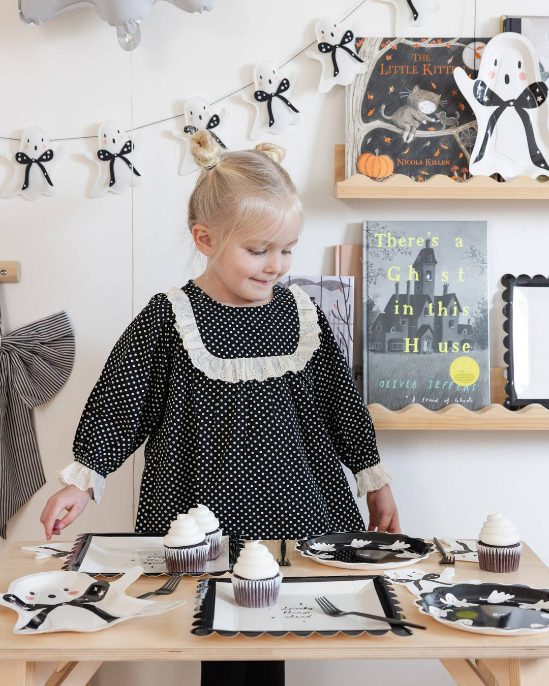 Halloween party setup with little girl and white felt ghost banner with black bows hanging on the wall
