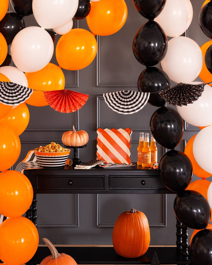 Black orange and white Halloween fan banner displayed with balloons and pumpkins above a Halloween party table