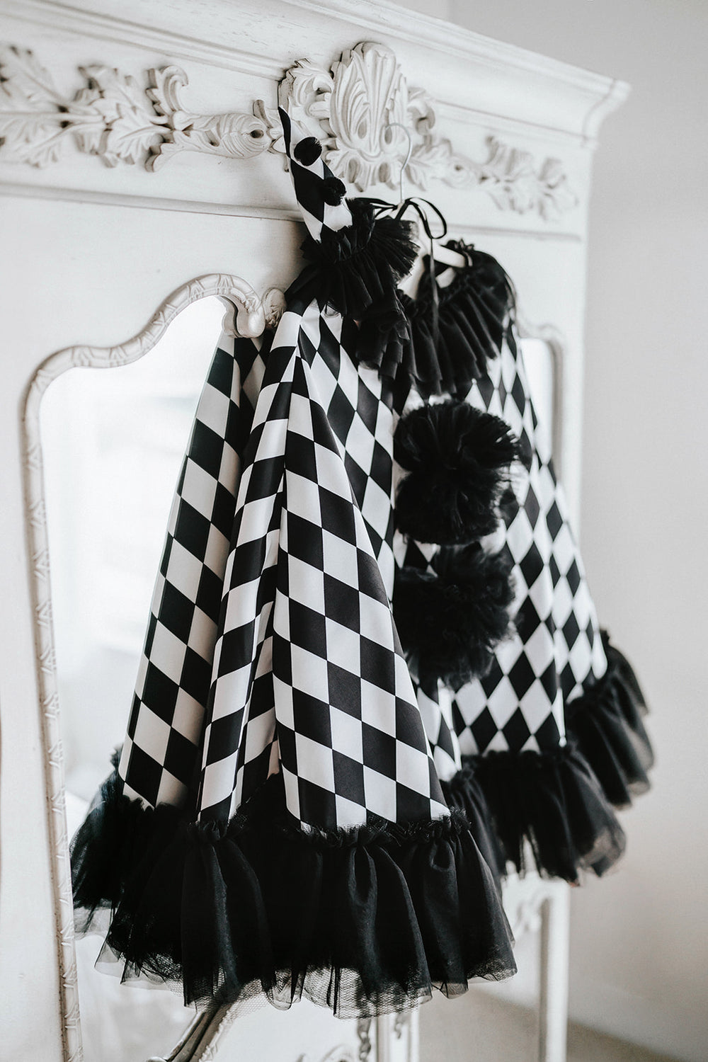 Pirouette black and white harlequin clown cape hanging on a closet with black tulle ruffles, pom-poms and matching pointed hat.