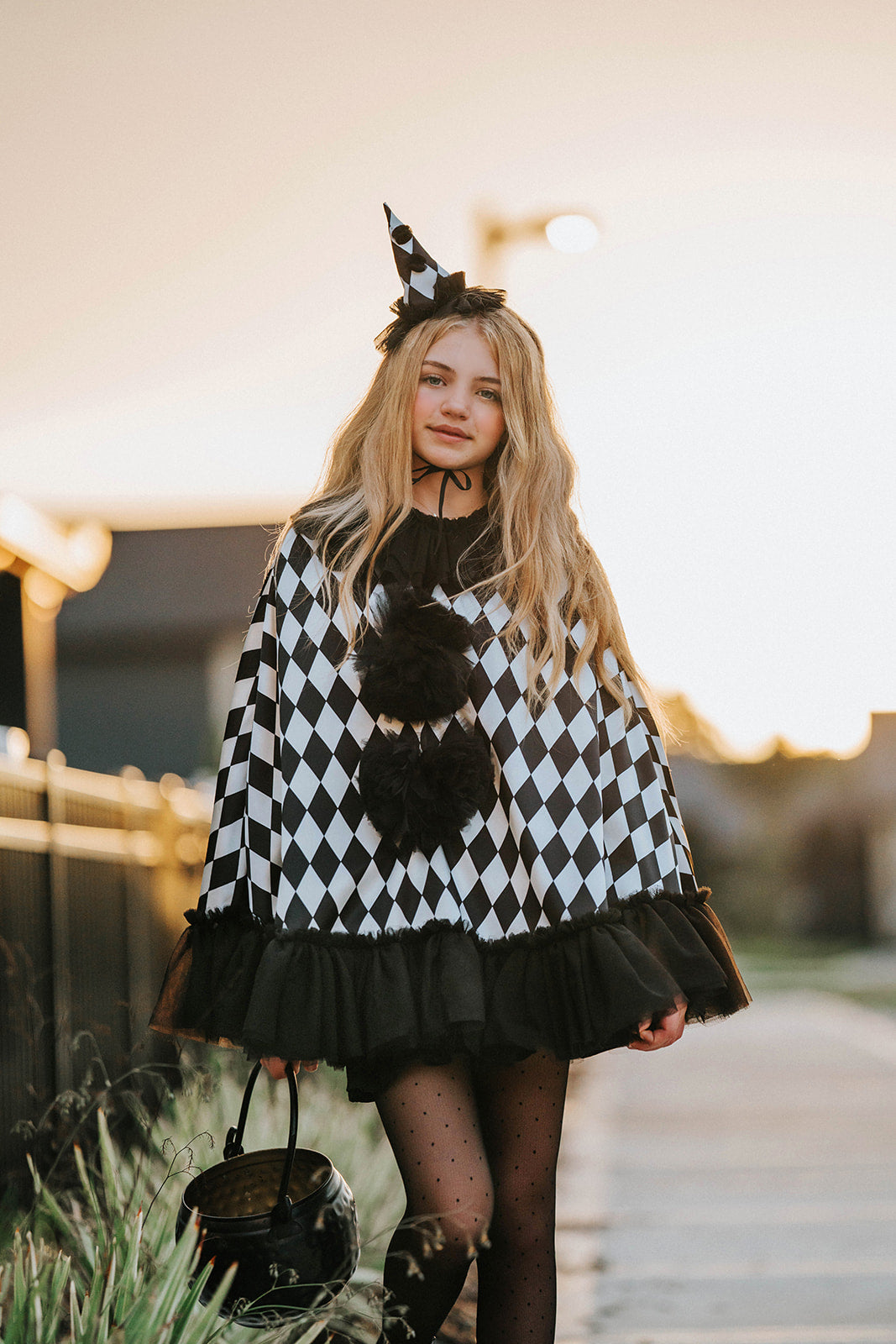 Teen wearing the Pirouette black and white harlequin clown cape with black tulle ruffles, pom-poms and matching pointed hat.