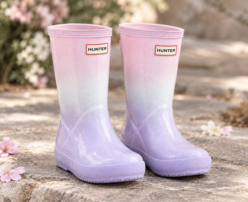 Hunter Boots Kids First Starcloud ombre rain boots facing forward on stone with a softly blurred floral background