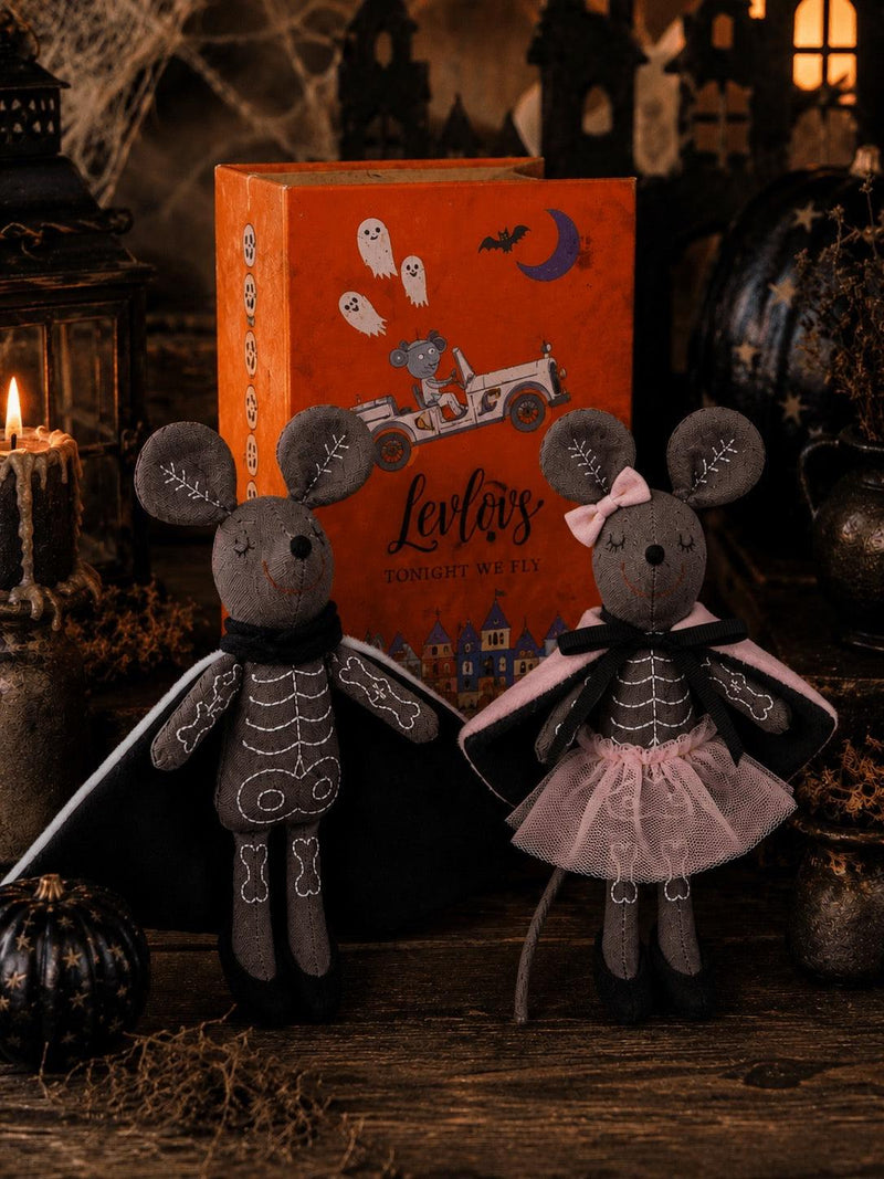 Two Halloween-themed plush mouse dolls dressed as skeletons, standing in front of an orange illustrated box labeled 'Levi's Zombie Witch'. The scene is styled with candles, cobwebs, and dark decorative props on a rustic wooden surface.