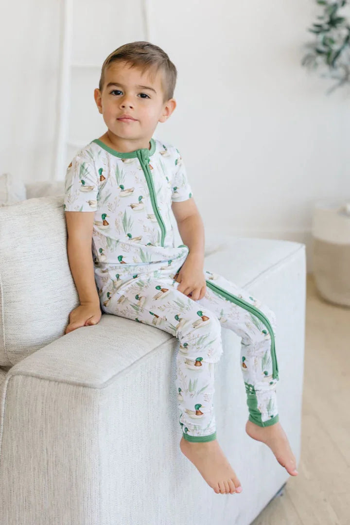 Little boy sitting on couch wearing mallard duck bamboo zipper pajamas with short sleeves and full zip.