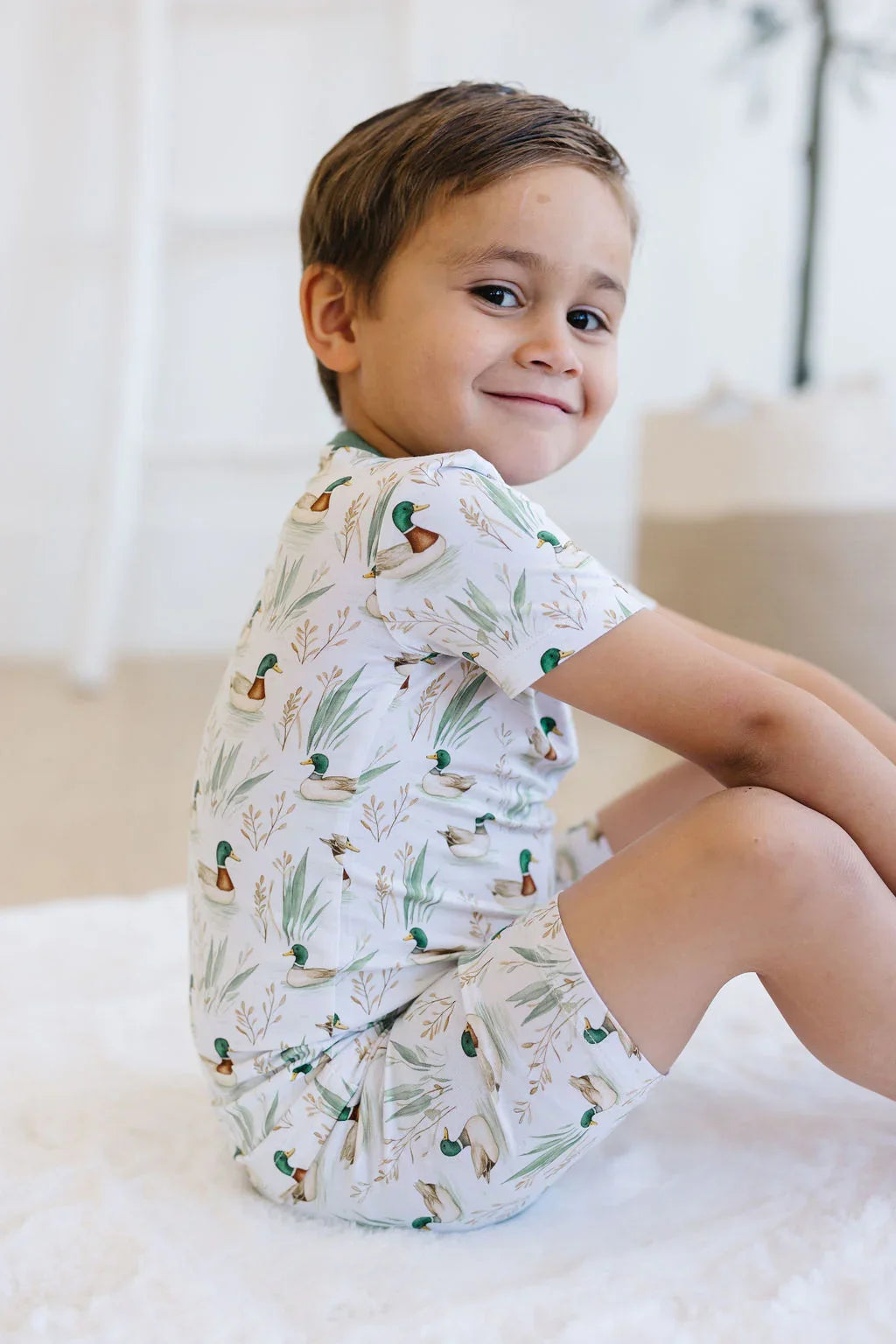 Toddler boy lounging in mallard duck bamboo pajamas, breathable two-piece sleepwear for summer.