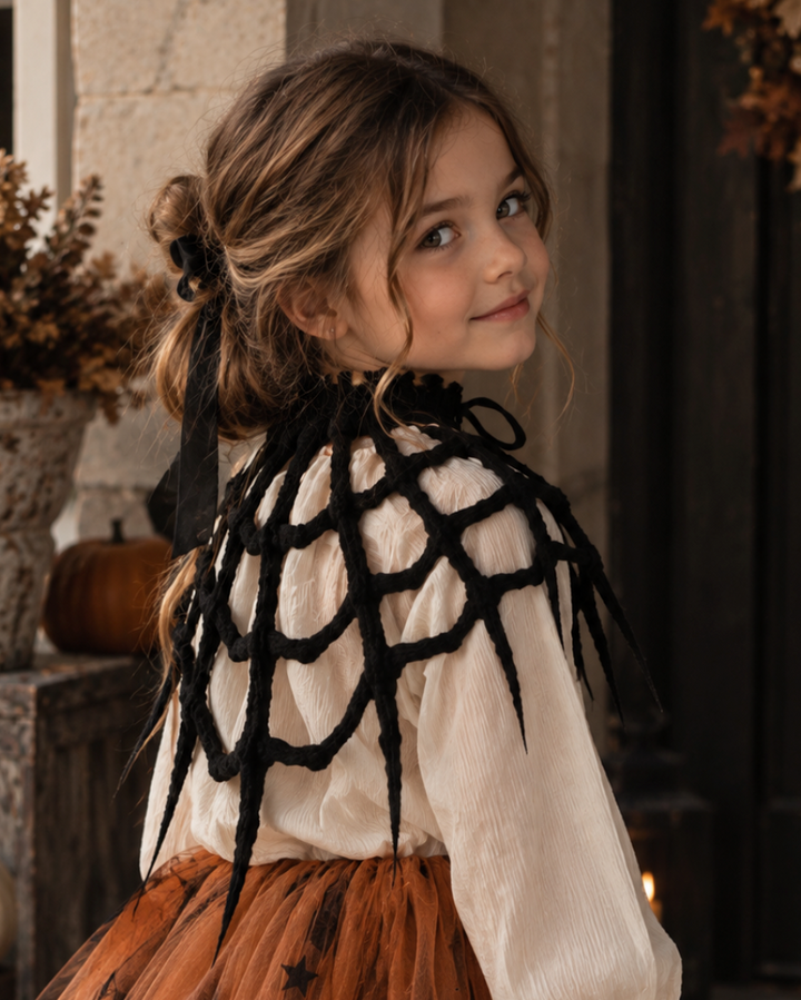 Child wearing black spiderweb capelet as part of a Halloween costume