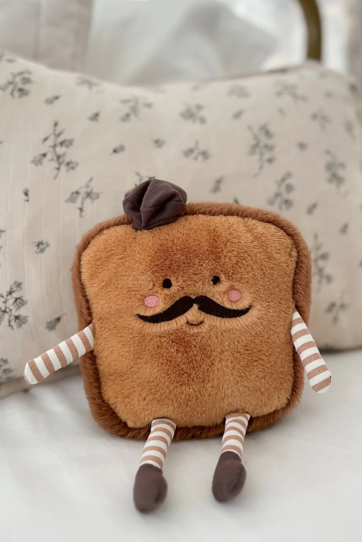Plush toy resembling rench toast  with a mustache on a floral pillow