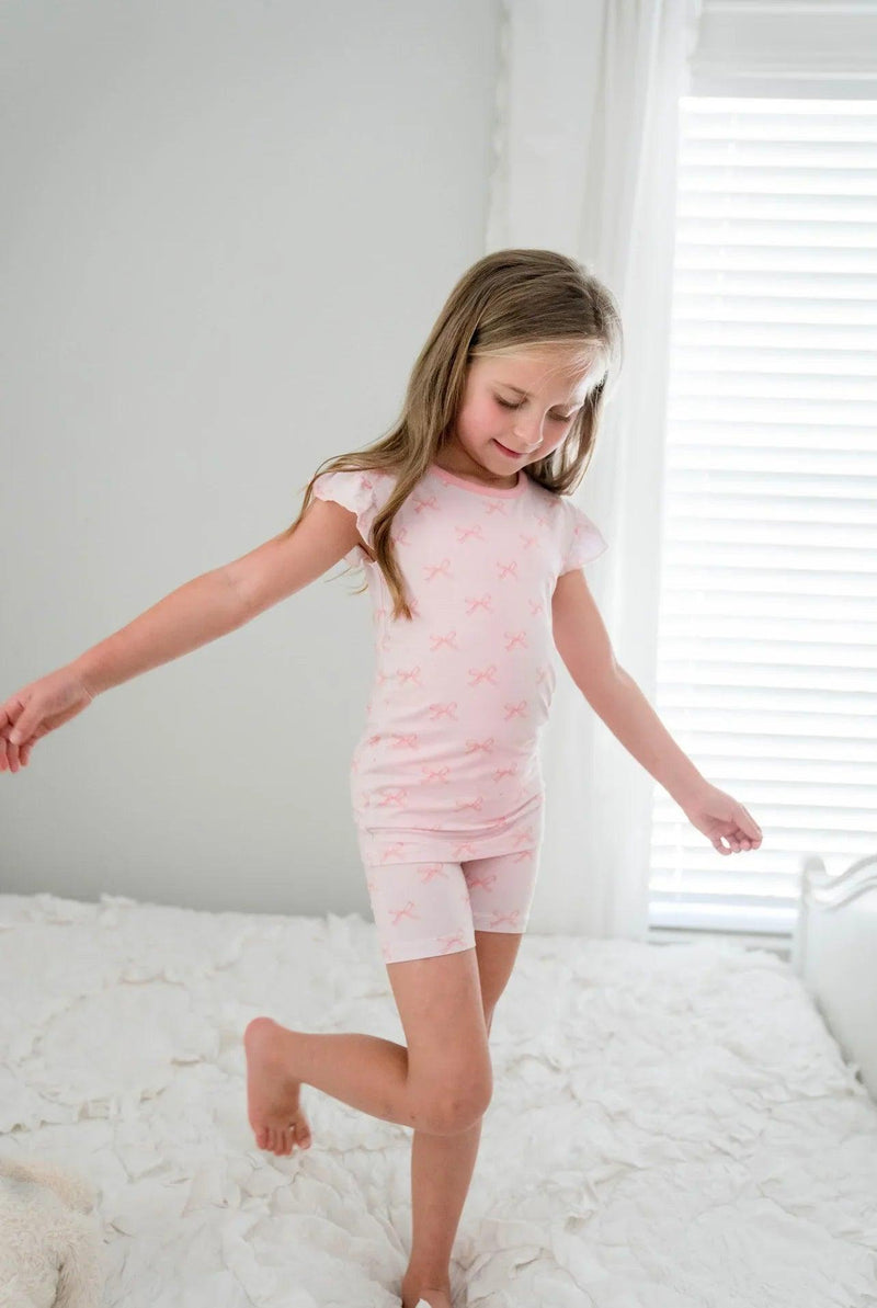 Side view of pink bows ruffle sleeve bamboo pajamas with shorts, shown on girl in casual standing pose.