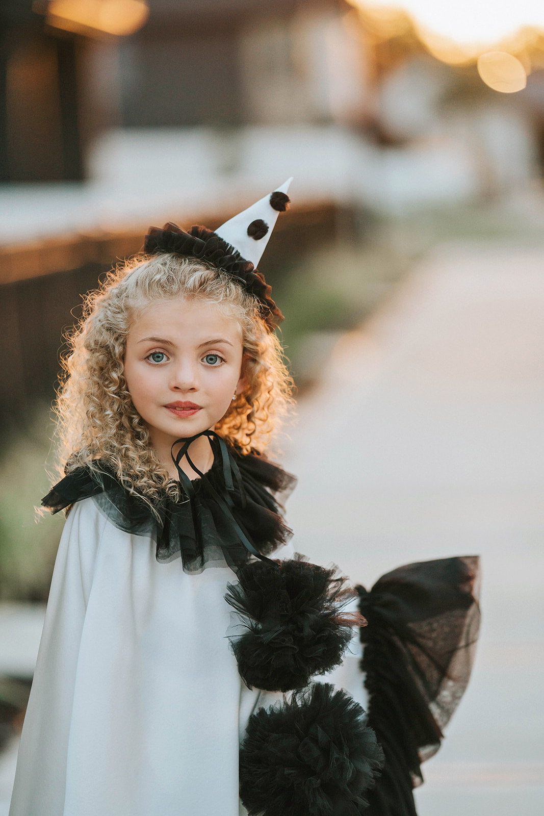Portrait of the Pirouette Pierrette clown costume featuring a white satin cape, black tulle neckline, pom-poms and pointed hat.