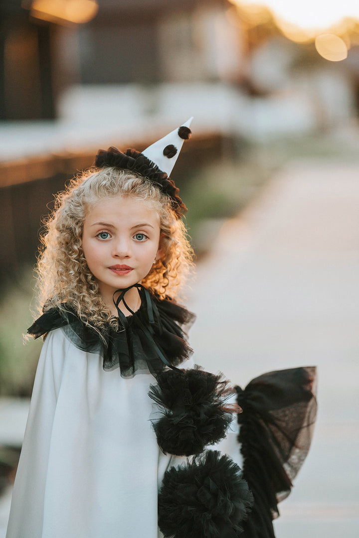 Portrait of the Pirouette Pierrette clown costume featuring a white satin cape, black tulle neckline, pom-poms and pointed hat.