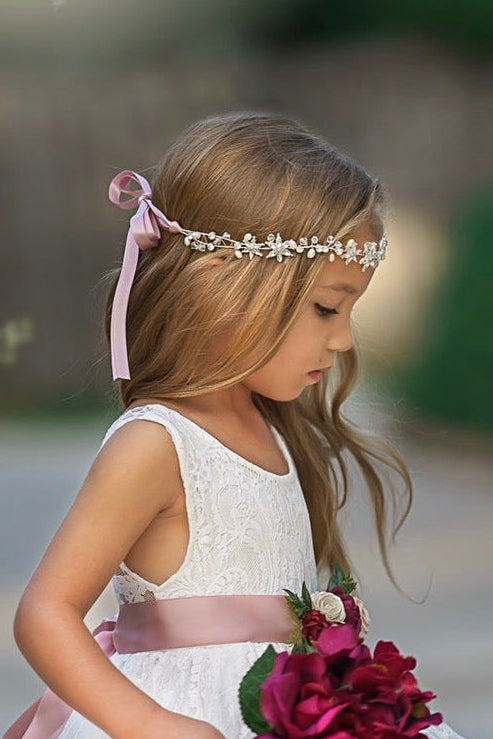 Soft white flower girl dress twirl photo showing lace movement and satin sash bow and silver crystal headband.