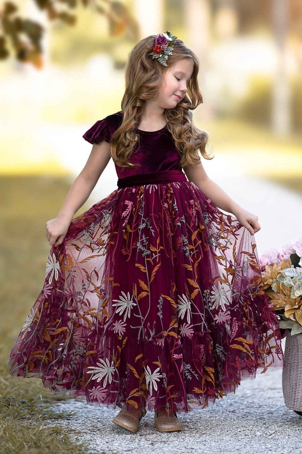 Girl wearing Virelle velvet flower girl dress in bordeaux with full-length embroidered tulle skirt outdoors