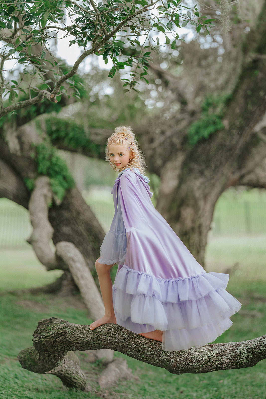 Girl wearing Amorette lavender Rapunzel-inspired princess cape with layered tulle ruffles in a woodland setting