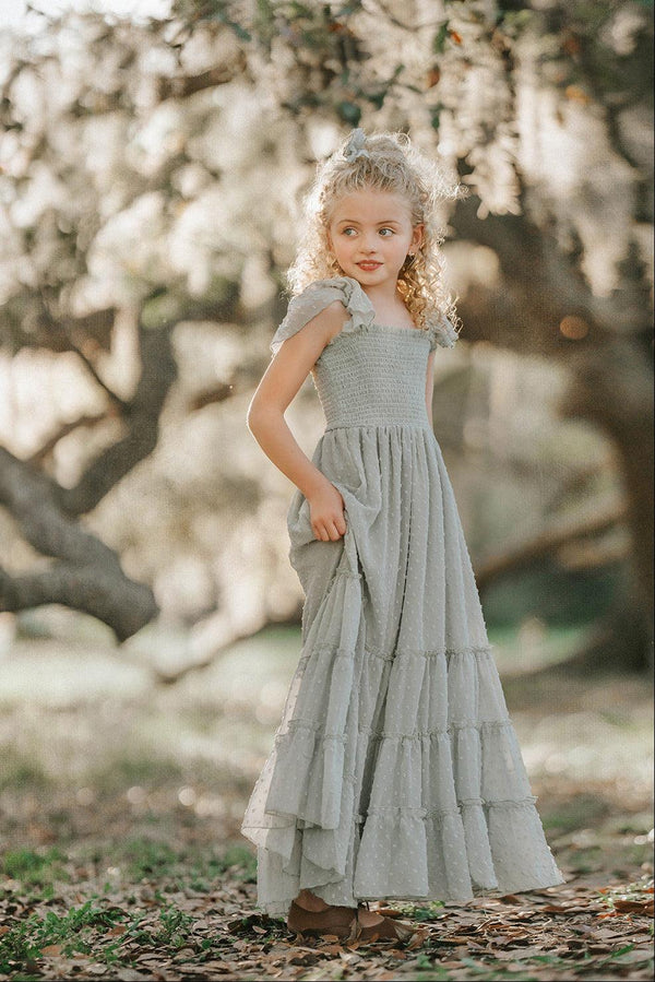 Girl wearing the Bay Leaf Orchard Collection dress in soft sage green Swiss dot fabric with a smocked bodice, flutter sleeves, and tiered heirloom skirt.