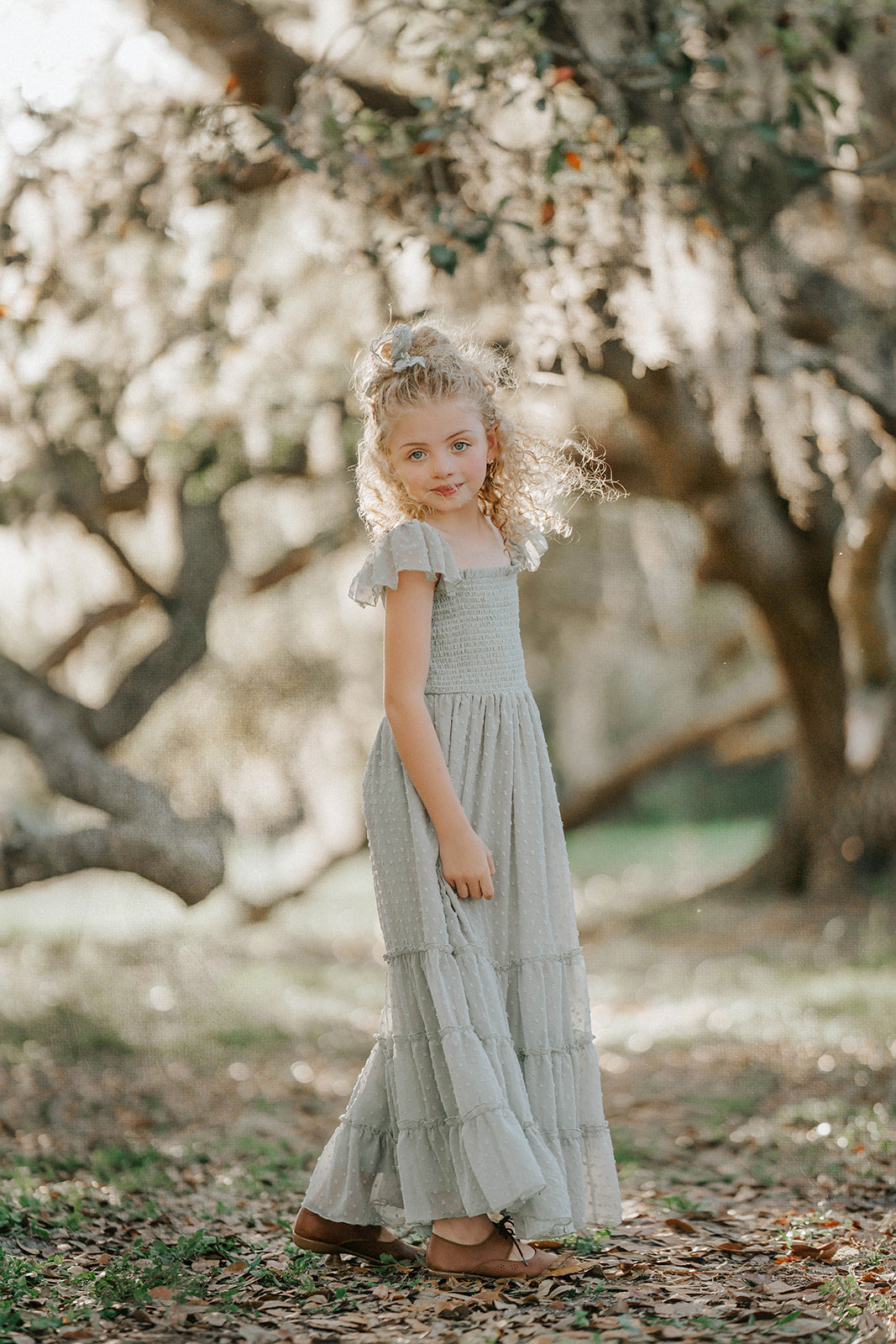 Full-length view of a girl wearing the Bay Leaf Orchard Collection dress featuring a smocked bodice and flowing tiered skirt.