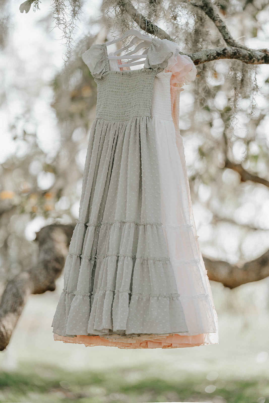 Bay Leaf Orchard Collection girls dress in soft sage green Swiss dot fabric hanging from an oak tree branch.