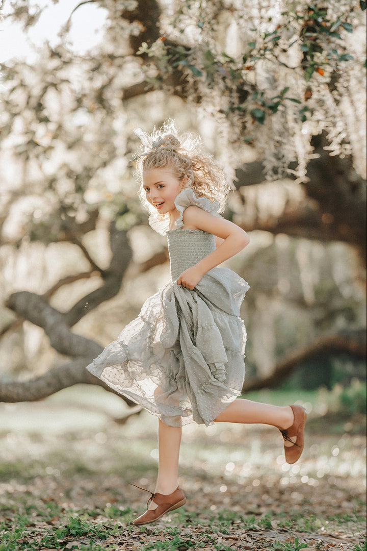 Girl walking through the orchard in the Bay Leaf Orchard Collection dress with a flowing tiered silhouette.
