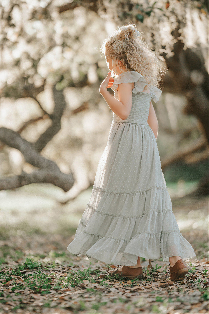 Side profile of a girl wearing the Bay Leaf Orchard Collection dress in sage green Swiss dot fabric.