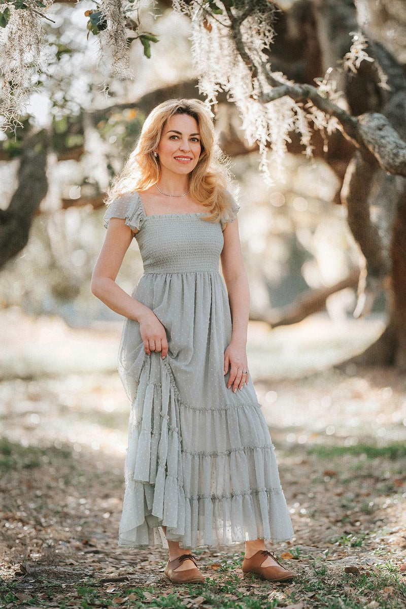 Woman wearing the Bay Leaf Swiss dot maxi dress by Autumn Moon Orchard Collection standing beneath moss-covered oak trees.