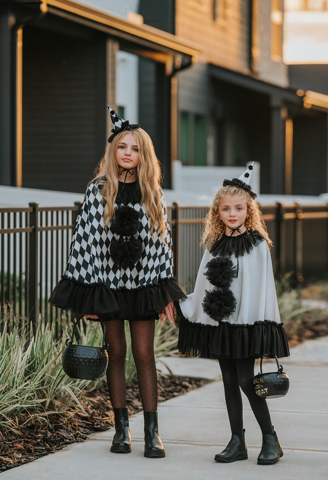 Child and teen wearing coordinating Pirouette clown capes and pointed hats from the black and white harlequin Halloween costume collection.